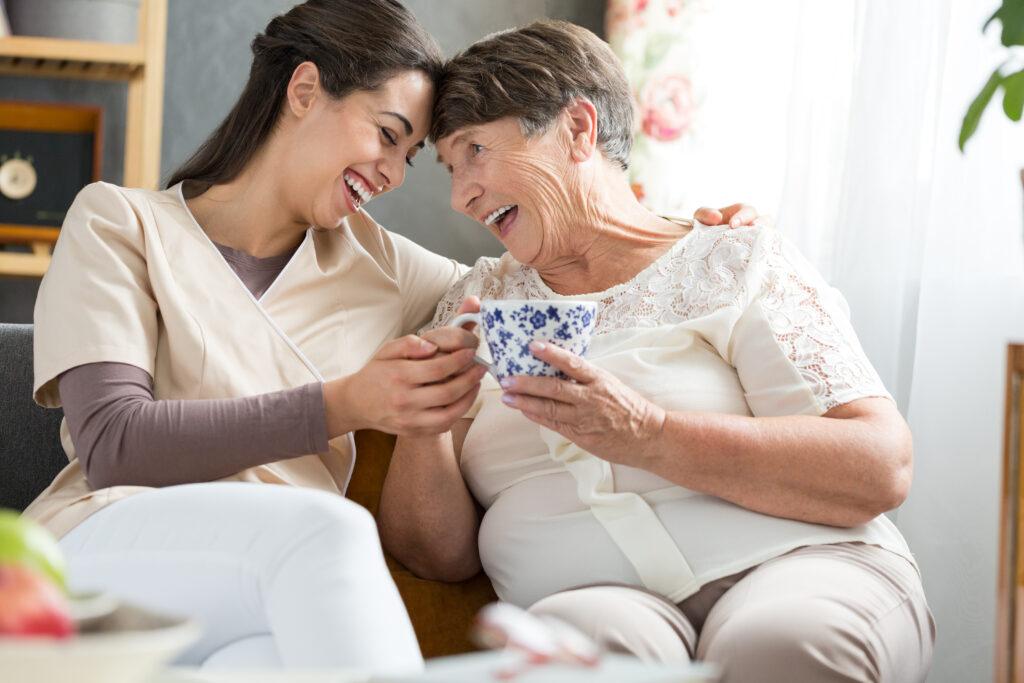 Roslyn Home Care personal caregiving services A caregiver sits and laughs with an elderly client over coffee personal care assistance